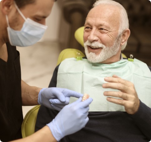 A dentist showing a denture to a smiling elderly patient